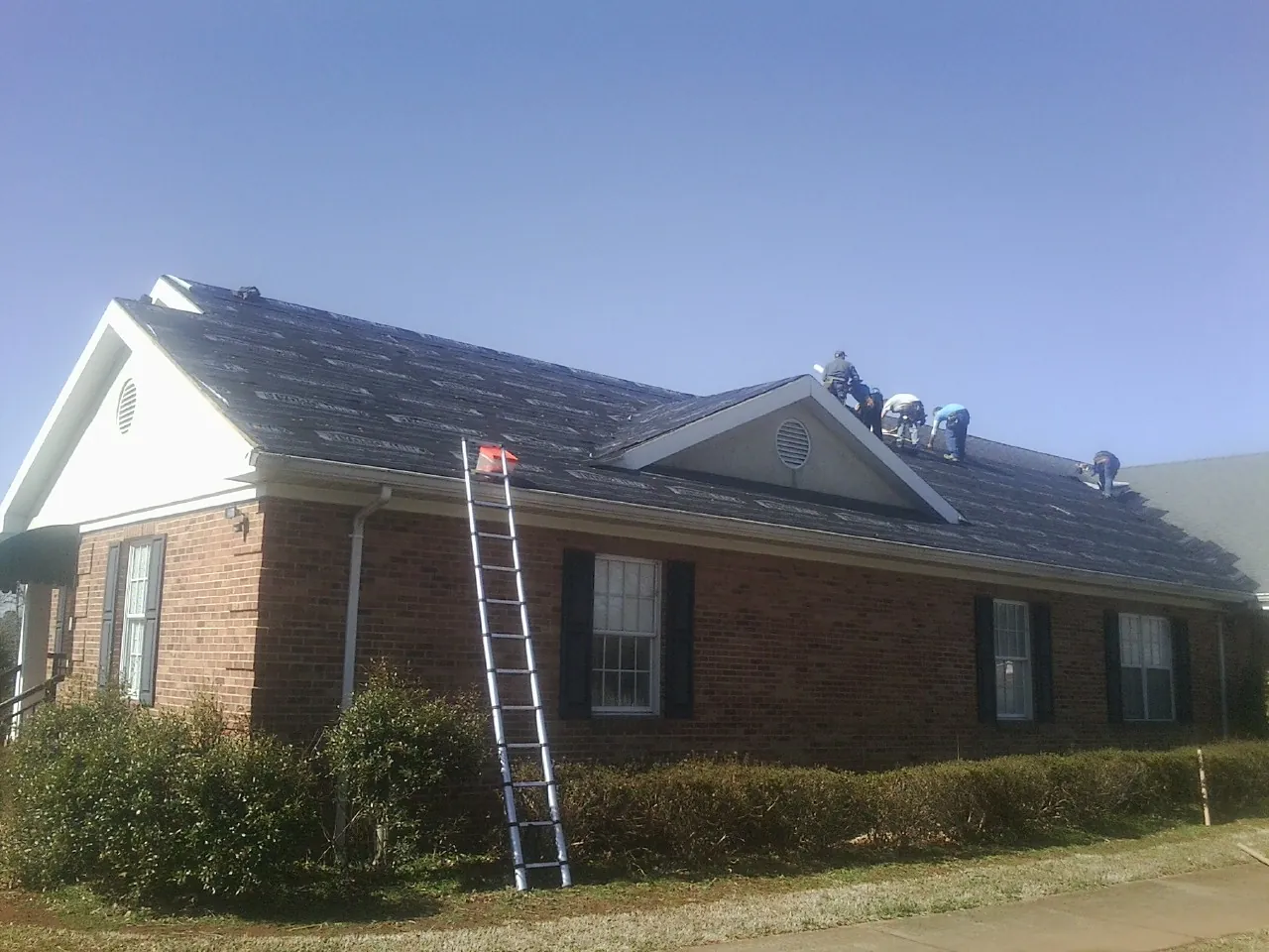 Crew tearing shingles off a brick ranch roof with a ladder set — Metal Roof Repair work by our crew in Armada