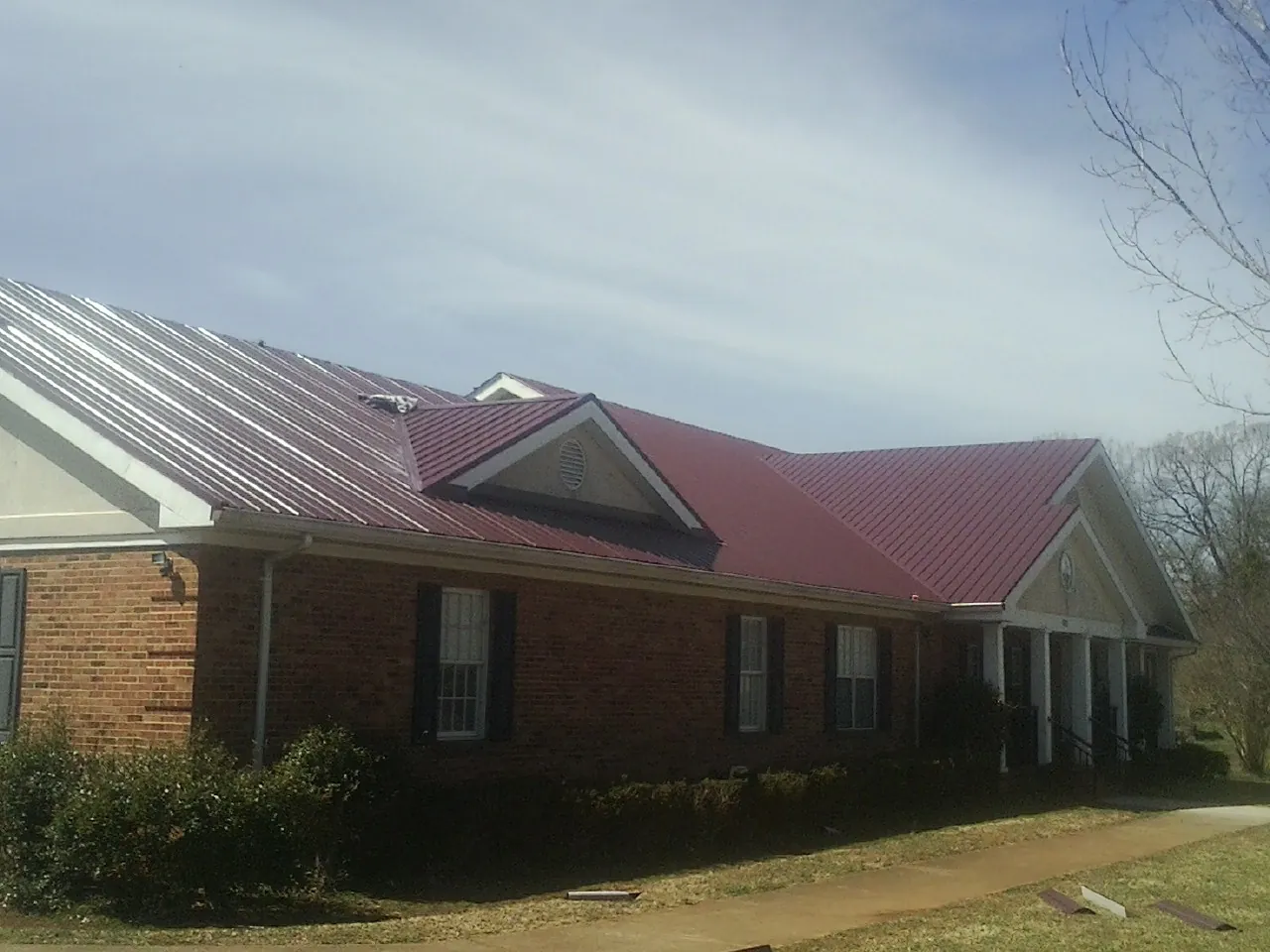 Red metal roof with gabled entries on a long brick building, from a Hail Damage Roof Repair job in Armada