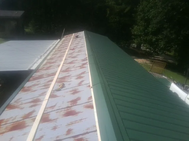 Old rusted panels beside newly installed green metal roofing — Wind Damage Roof Repair by Roofing Brothers in Armada