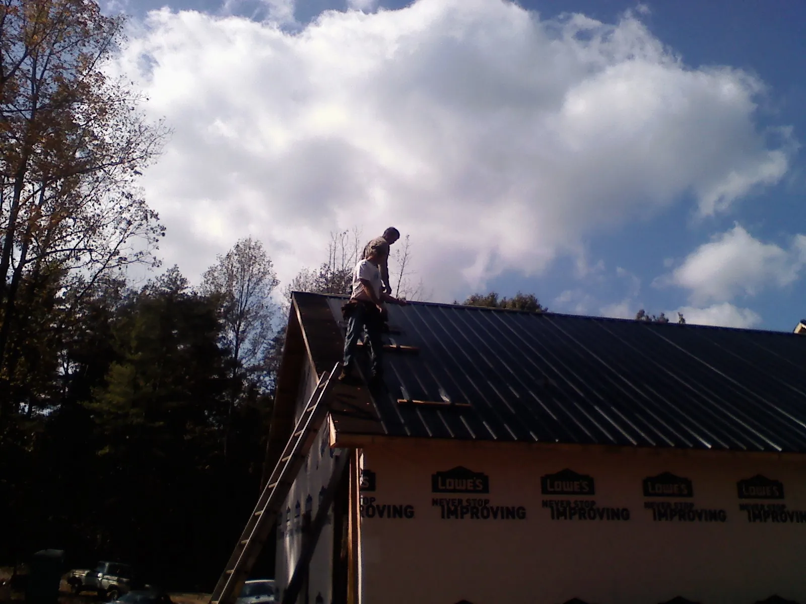 Roofer fastening dark metal panels high against a cloudy sky, from a Roof Inspection job in Armada